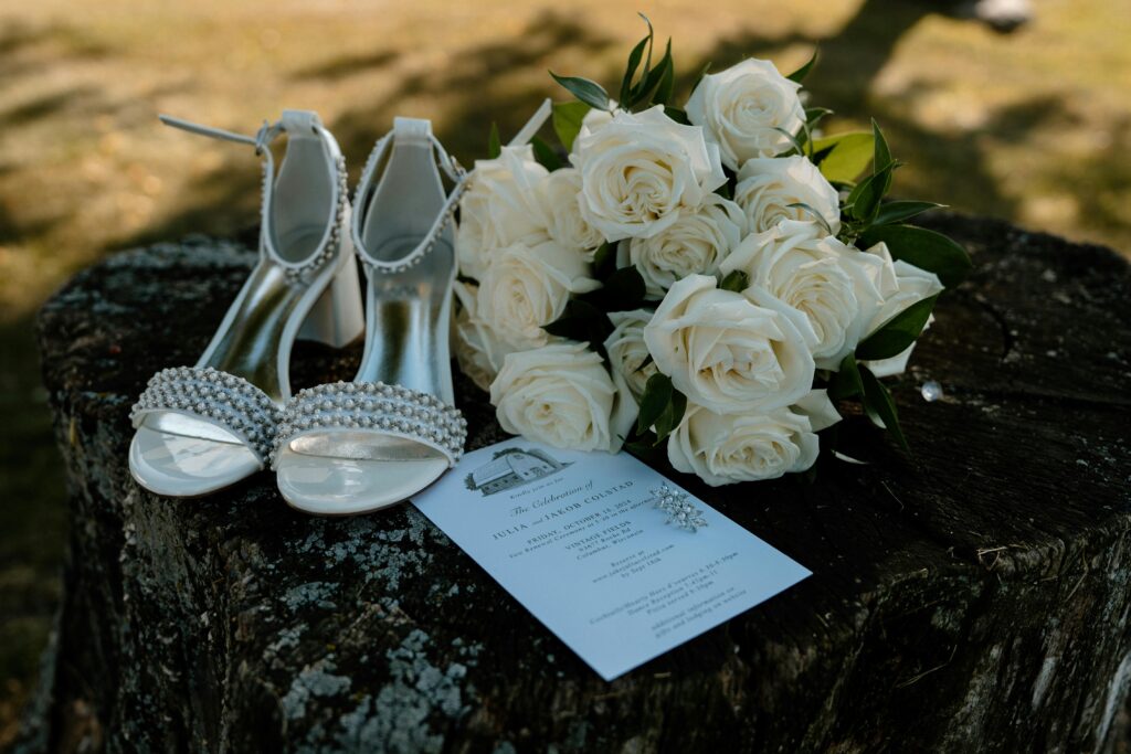 White roses, bridal shoes, and invitation on rustic wood. Perfect for wedding themes.